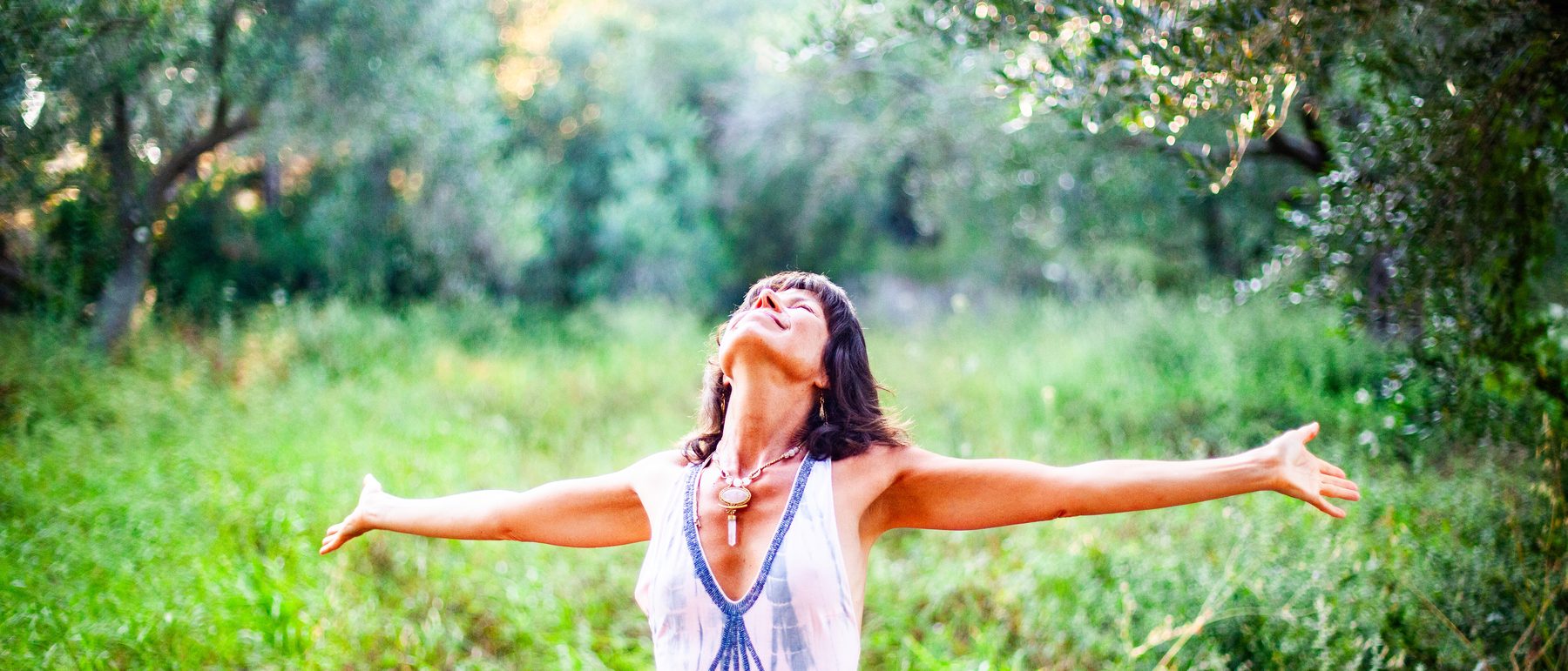 Dr. Melanie Hernand Shine standing with arms open in a sunlit meadow